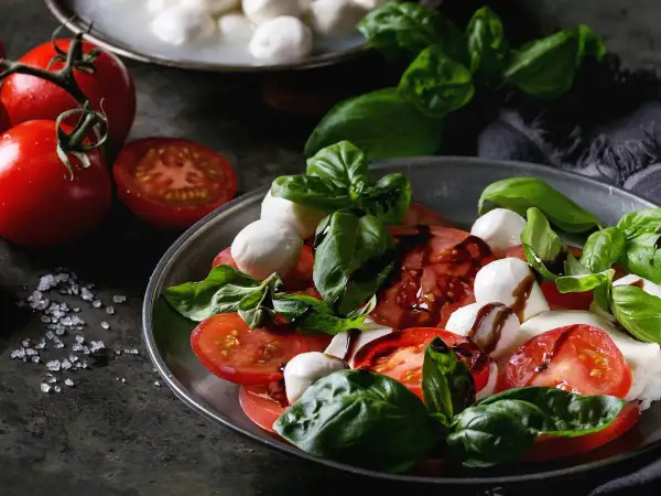 Sałatka caprese: soczyste pomidory, białe kulki mozzarelli i świeża bazylia, polane ciemnym sosem.