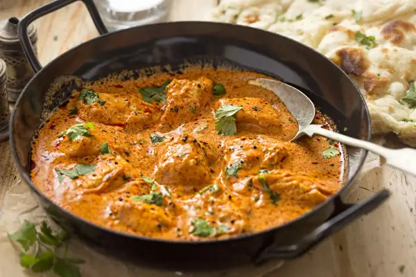 Aksamitny kurczak w sosie na bazie przyprawy curry, udekorowany świeżą kolendrą, podany z chlebkiem naan.