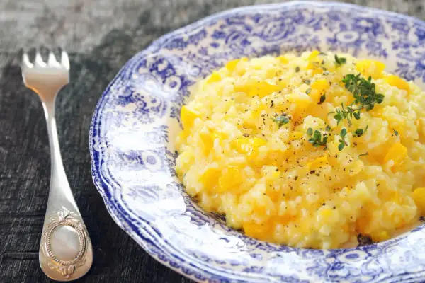 Pyszny, kremowy ryż do risotto z kawałkami dyni, posypany świeżym tymiankiem i pieprzem. Obok leży elegancki widelec.
