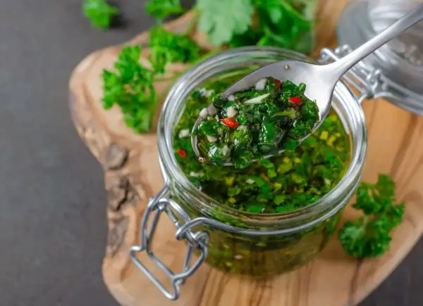 Łyżka z aromatycznym chimichurri, pełnym ziół i chili, nad słoikiem pełnym tej zielonej, pysznej pasty.