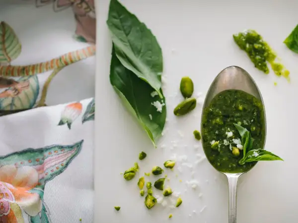 Łyżka pełna aromatycznego pesto z rukoli, obok pistacje i listki bazylii.
