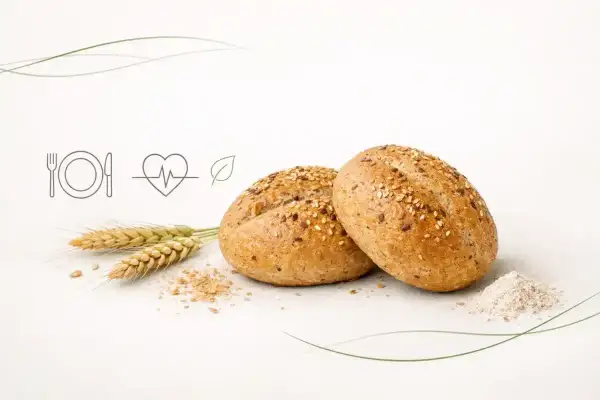 Dwie bułki grahamki posypane sezamem i siemieniem lnianym, obok kłosy zboża i garść mąki. Symbol zdrowego odżywiania.