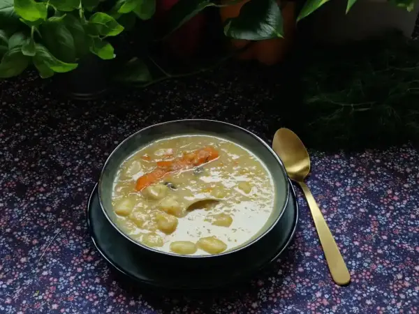 Aromaticzna zupa na żeberkach z kawałkami marchewki i ziemniaków, podana w misce obok złotej łyżki.